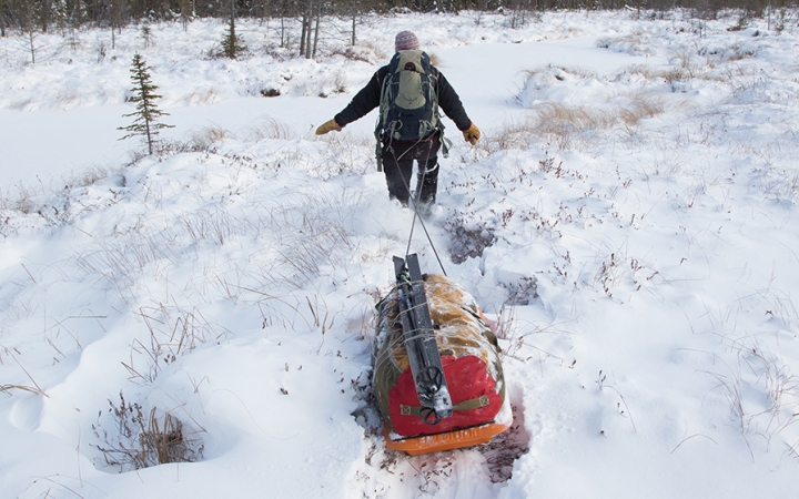 A person wearing a backpack pulls a small sled behind them through deep snow